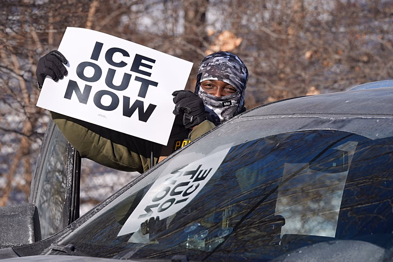 FÁJLÉK: Egy szövetségi tiszt feltart egy „ICE Out Now” feliratú táblát a forgalom leállása közben, 2026. január 27.