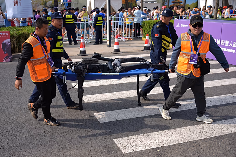 A biztonsági személyzet és a résztvevők hordágyon hordozzák a robotot, miután az részt vett a Peking E-Town Félmaratonon és a Humanoid Robot Félmaratonon