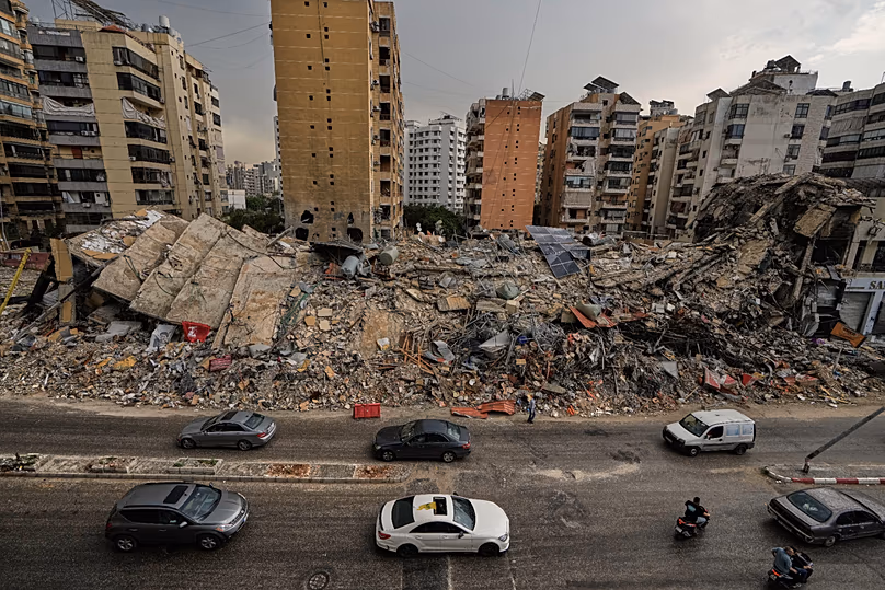 Lakosok elhaladnak az elpusztult épületek romjai mellett Dahiyehben, 2026. április 17.