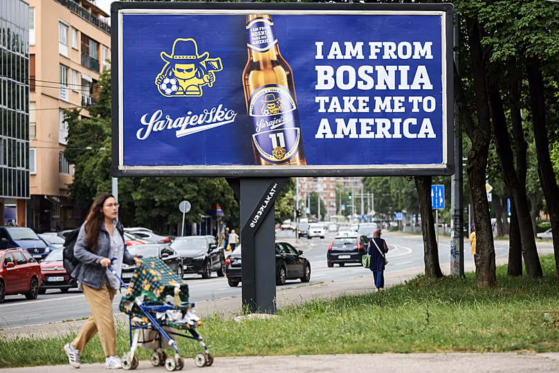 Egy nő elmegy egy hirdetőtábla mellett, amelyen a Dubioza kolektiv „I Am From Bosnia, Take Me to America” című dalának szövege látható Szarajevóban, 2026. június 11.