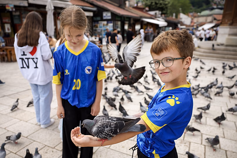 Gyerekek boszniai válogatott mezben etetik a galambokat Szarajevó óvárosában a 2026-os labdarúgó-világbajnokság Kanada–Bosznia mérkőzése előtt, 2026. június 12.