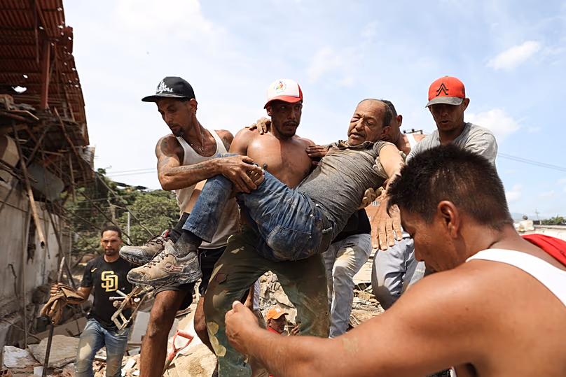 A szomszédok szállítanak egy férfit, akit egy összedőlt épület romjai közül mentettek ki a venezuelai La Guairát sújtó földrengés másnapján, 2026. június 25-én, csütörtökön.